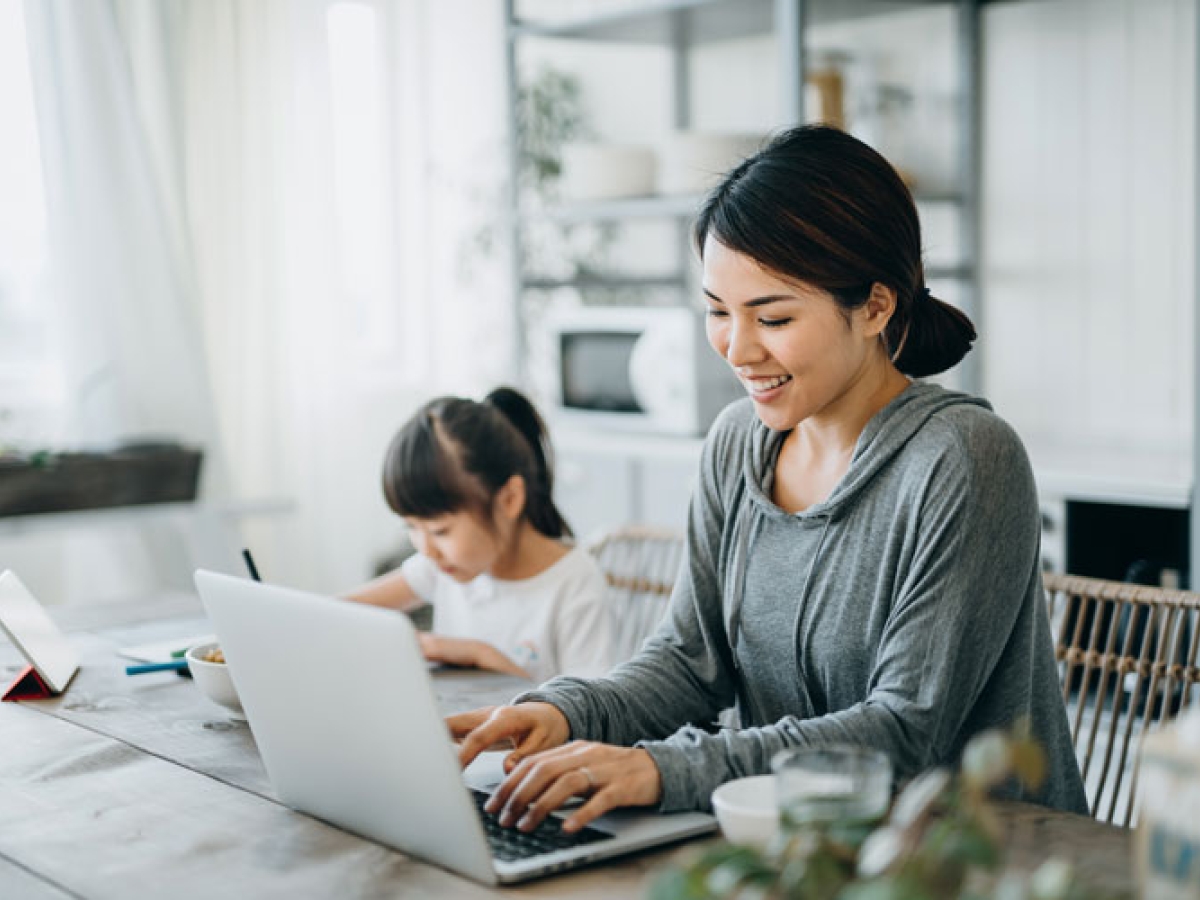 Woman sitting at the table on her computer with her daughter sitting next to her Woman sitting at the table on her computer with her daughter sitting next to her