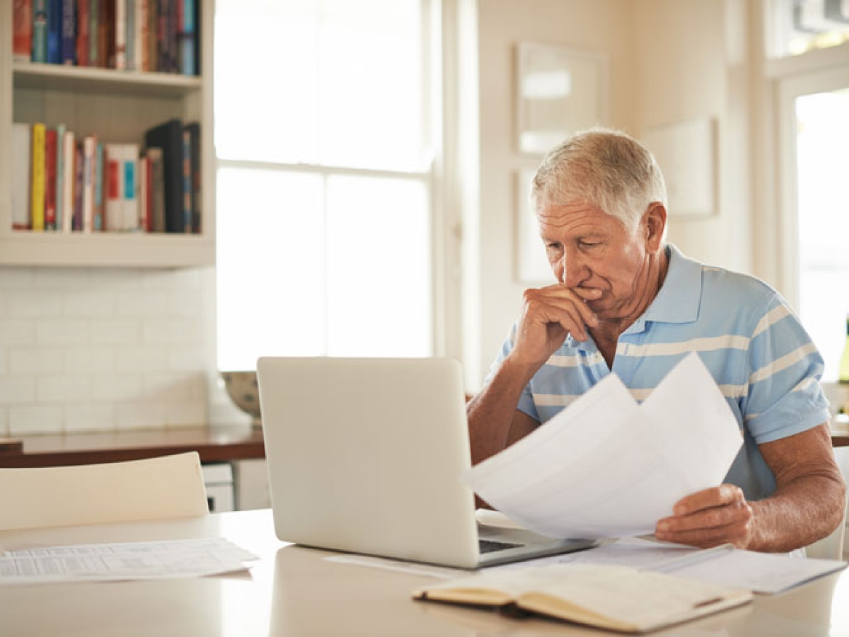 Elderly man concentrating on his paperwork and sitting in front of his laptop